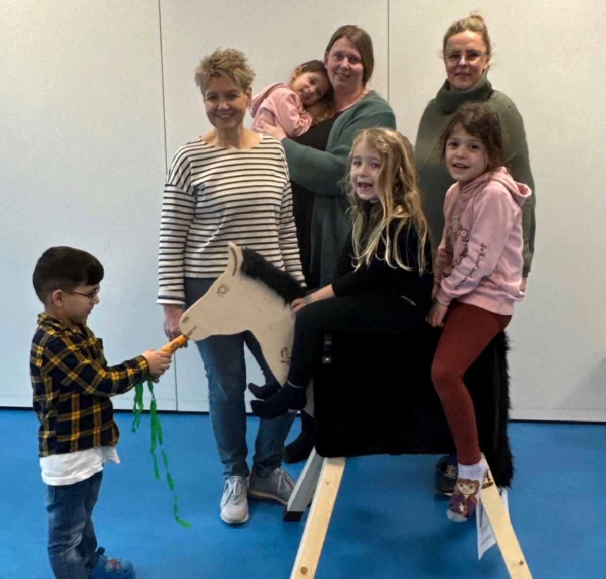 Antje Koch (hintere Reihe links) und Imke Hüter-Dannehl (rechts) vom Club Soroptimist Einbeck-Northeim übergeben ein Holzpferd an die Kinder des Kindergartens Münstermauer in Einbeck. Die Erzieherin Stefanie Beise (Mitte) sieht freut sich, dass das Pferd Amadeus gleich mit einer selbstgebastelten Möhre gefüttert wird.